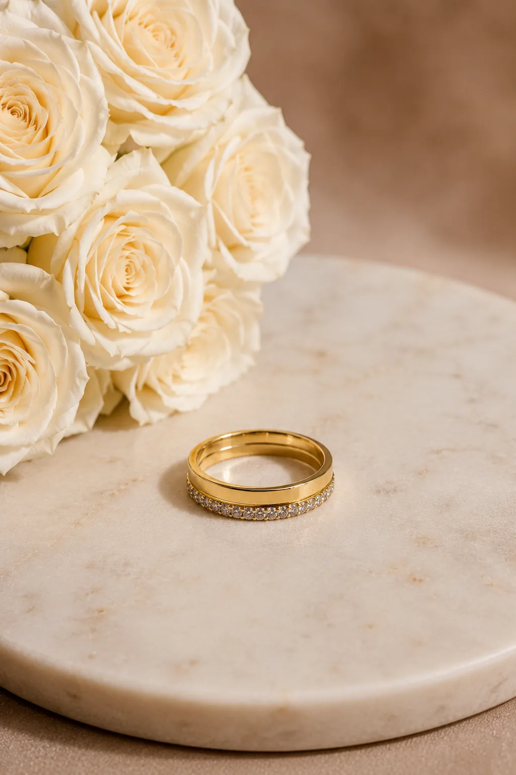 Gold pavé wedding band beside a bouquet of white roses on marble